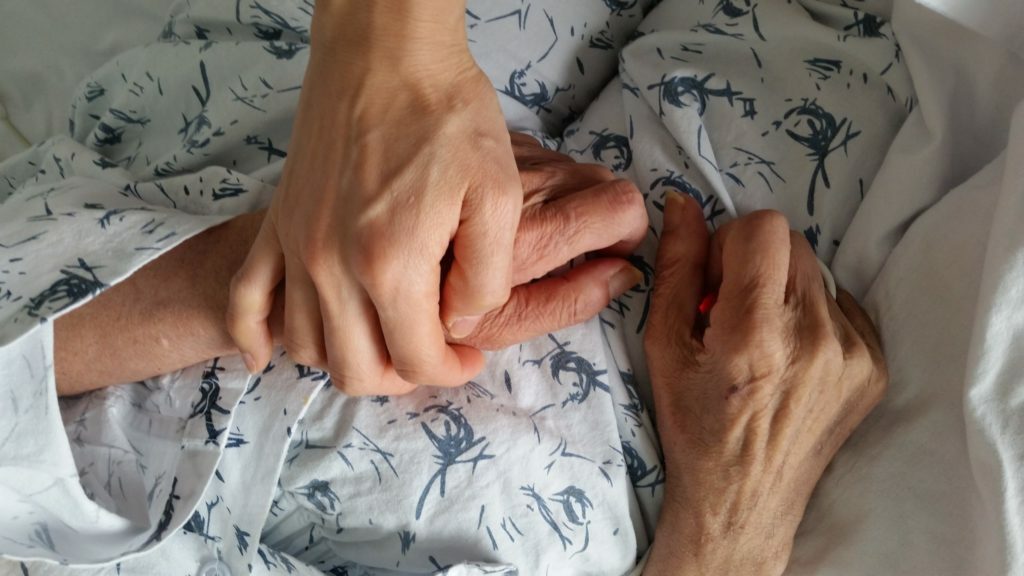 holding elderly family member's hand in hospital during end of life care