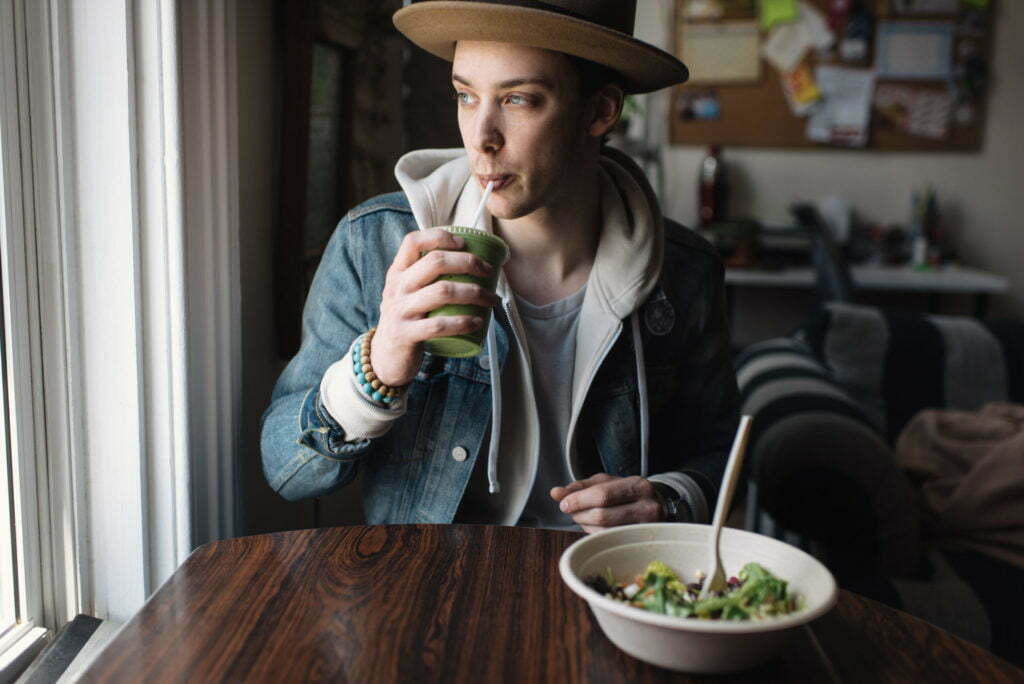 Young man sitting at table, having meal, drinking health drink